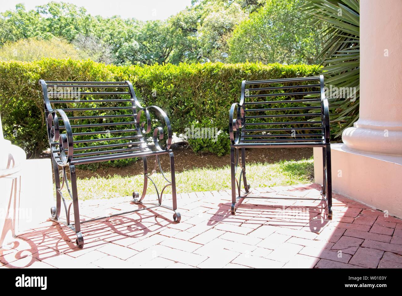 Two wrought iron chairs sit on a brick patio overlooking beautifully landscaped lawn Stock Photo