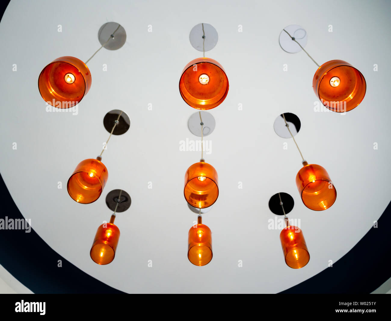 Modern orange ceiling lamp hanging from round white ceiling. Lighting