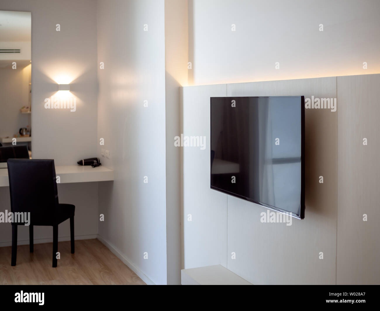 Black LED television on white wall near makeup corner with black chair in front of the mirror in hotel room. Stock Photo