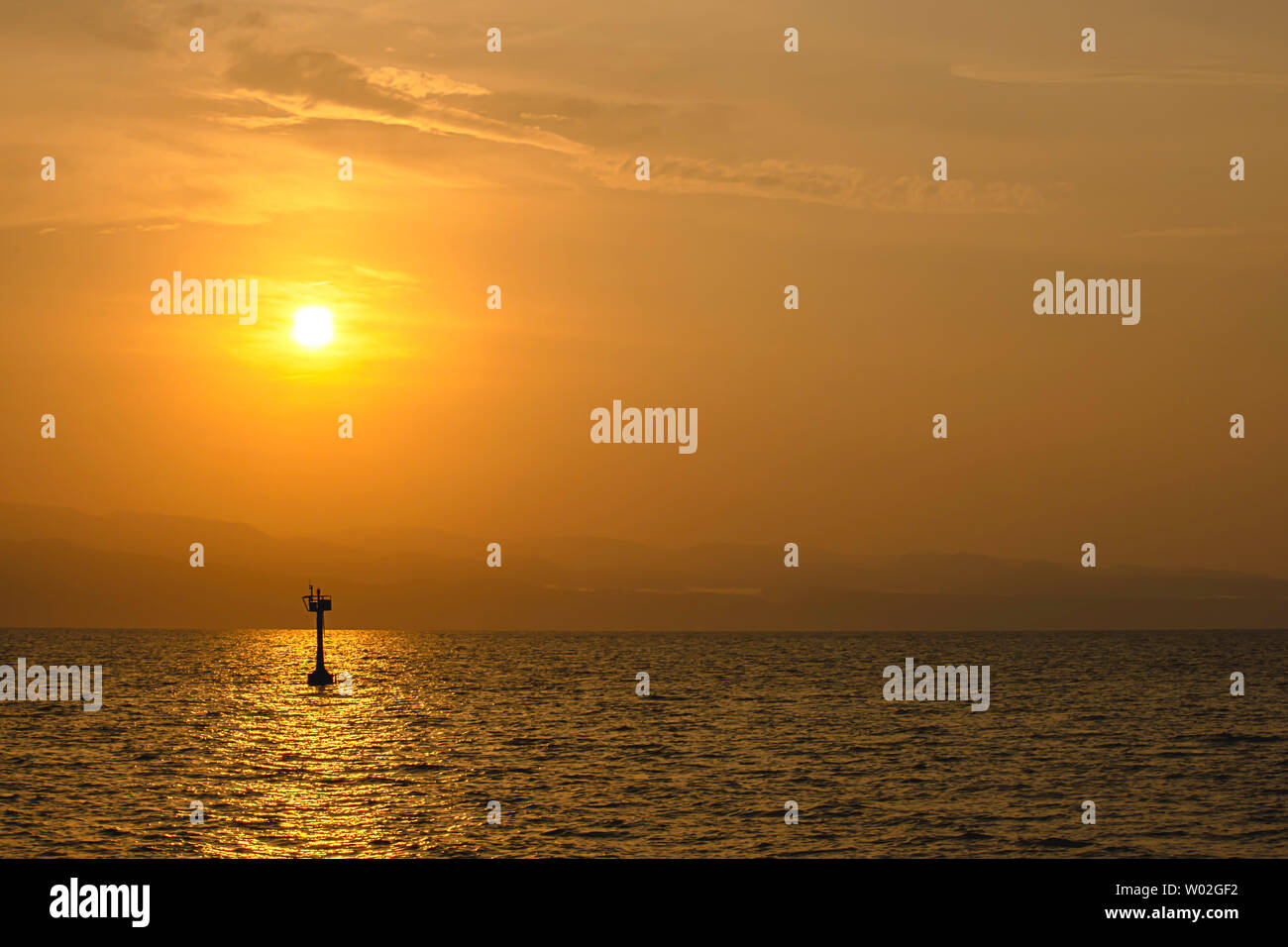 Golden light of sunrise behind the mountains and the shadow of signal lamp for sailing in the sea. Stock Photo