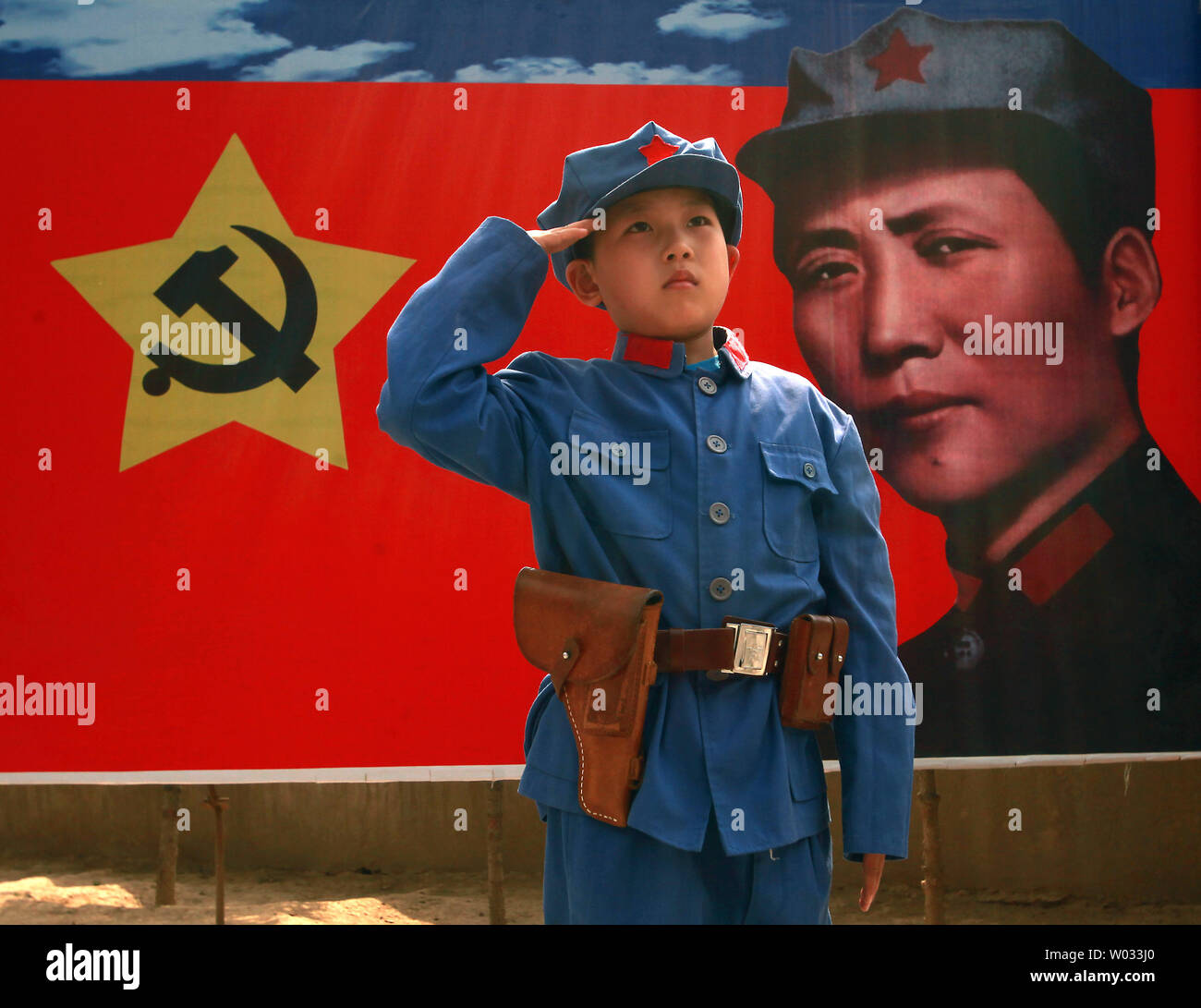 A Chinese boy dressed in a communist uniform poses for a photo, in front of  a banner of the communist party's ideal soldier Li Feng, at a site used by  former helmsman