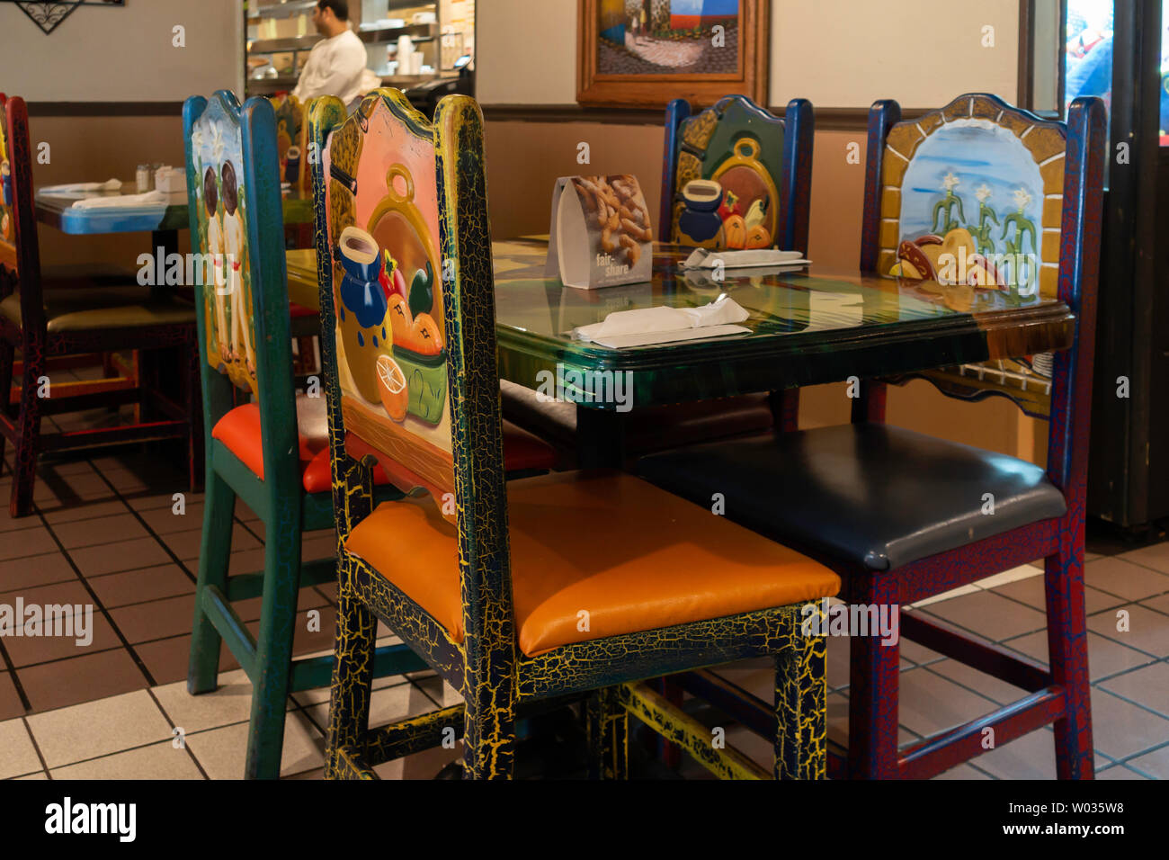 Decor of a Mexican restaurant showing colorfully designed chairs, tables and Mexican decor. Cook in the background. Arkansas, USA. Stock Photo