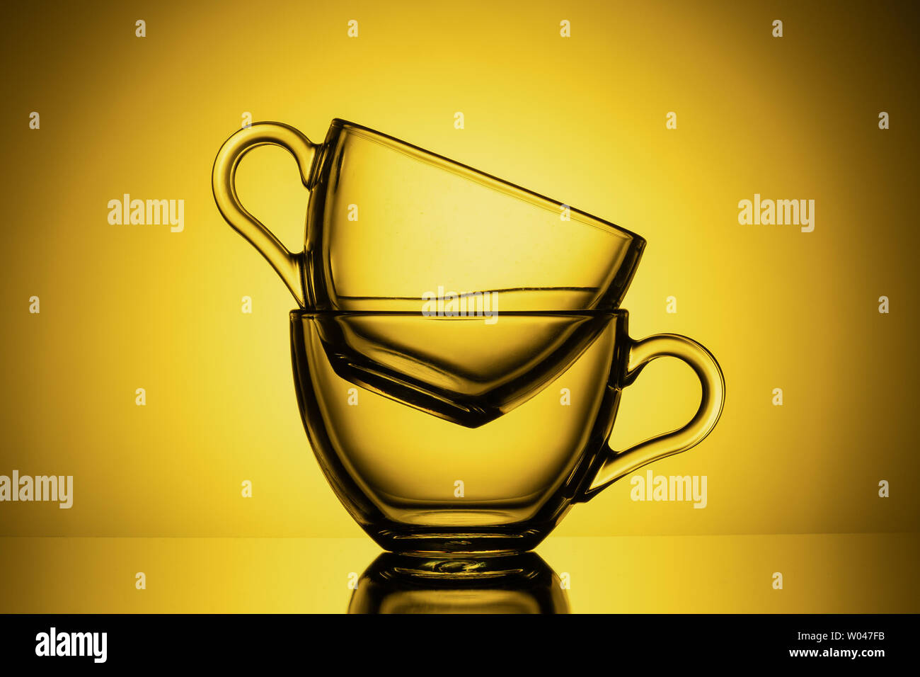 Two transparent glass mugs for tea. Yellow background, close-up, HORIZONTAL LAYOUT Stock Photo