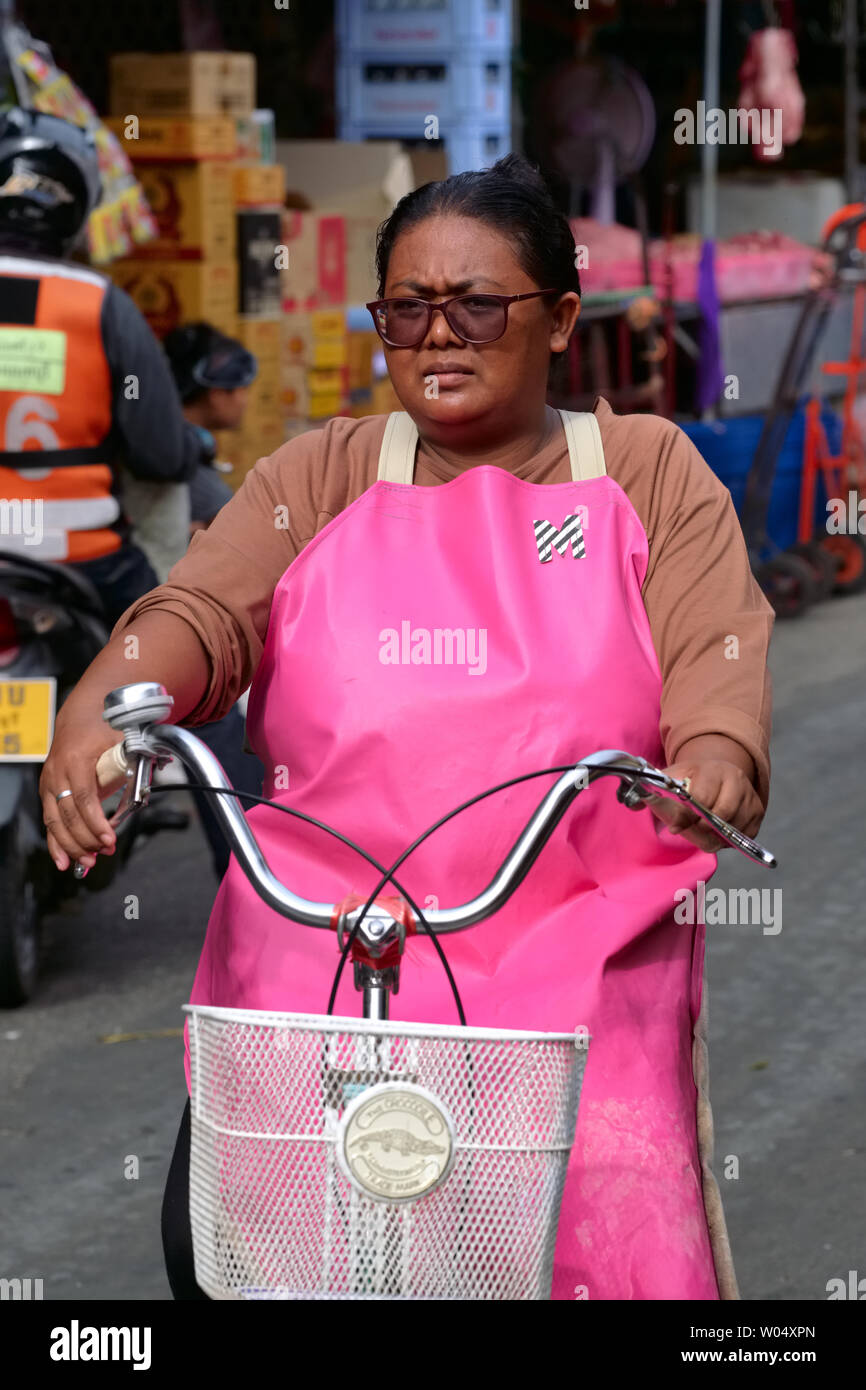 A market vendor in Nonthaburi, Thailand, on an errand cycling through her market Stock Photo