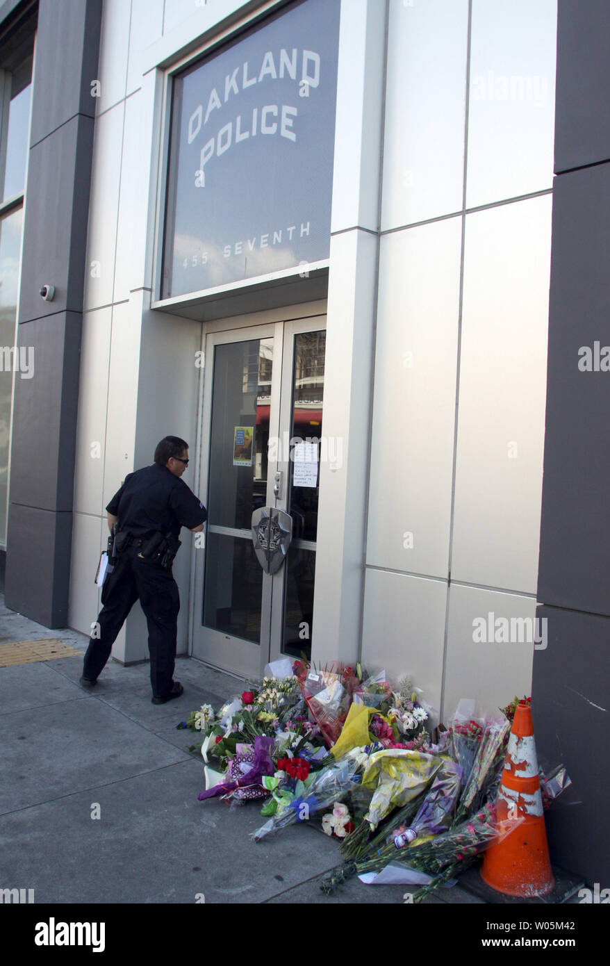 An Oakland police officer walks by a growing number of flowers on March 22, 2009, in front of the Oakland Police department in memory of the four Oakland Police officers shot to death on March 21 in Oakland, California. A parolee shot to death three police sergeants within two hours during a traffic stops. The fourth officer died from gun shot wounds Sunday morning at the Highland hospital in Oakland.   (UPI Photo/Bob Larson) Stock Photo