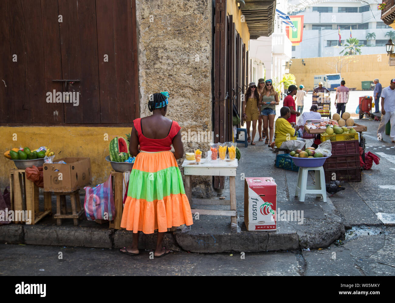 A woman in a colorful, bright dress sells fruit at a street stand on the streets of Cartagena, Colombia, in the historic center (Centro). Stock Photo