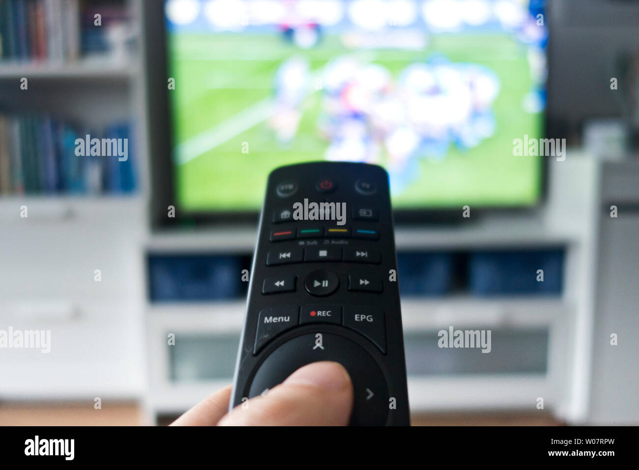 man holding a remote control pointed at the TV screen showing some sport event Stock Photo