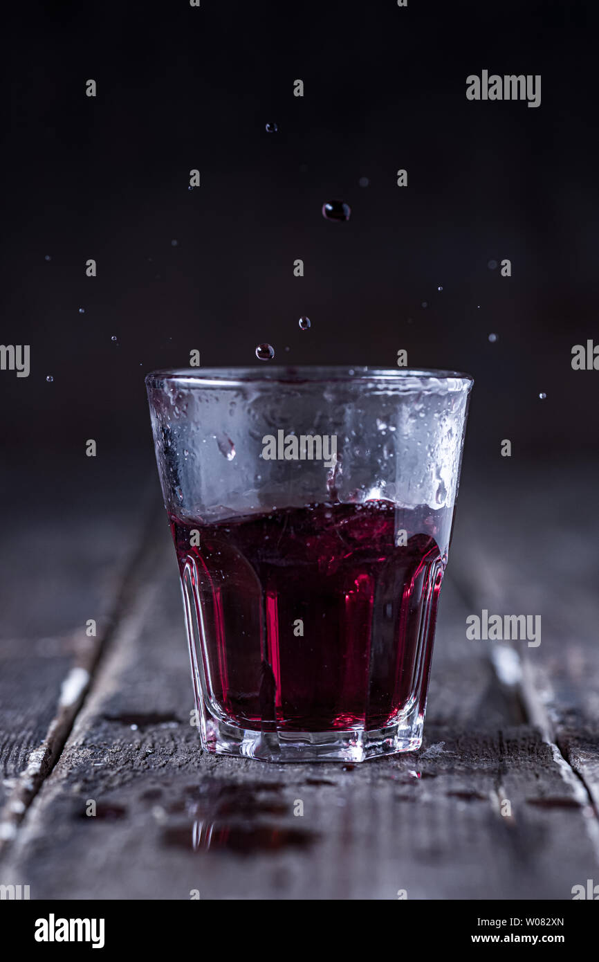 Shot of Red Bitter Liquor with Drops Splashing on Wood Stock Photo