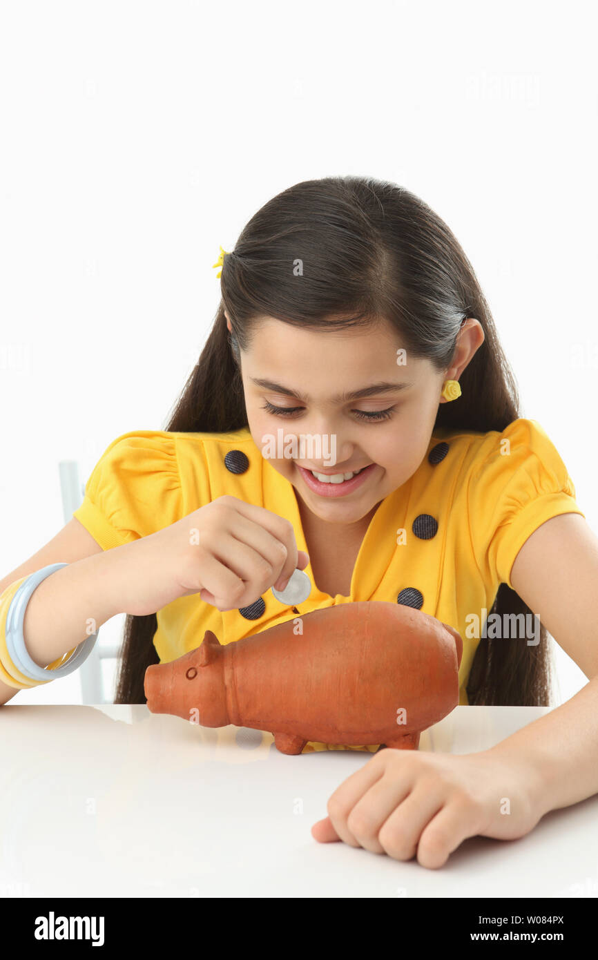Girl inserting coin into a piggy bank and smiling Stock Photo - Alamy