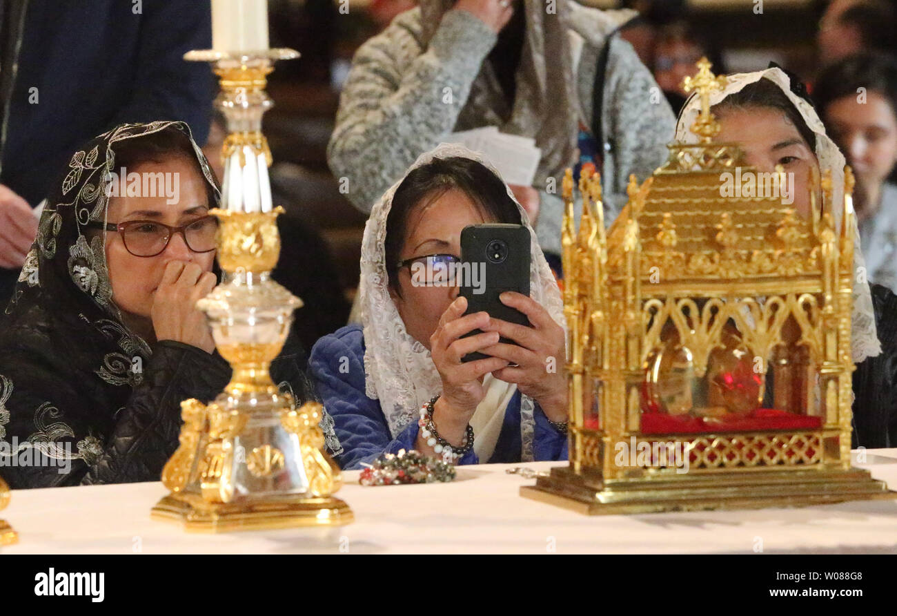A parishioner makes a photo with her phone while kneeling to pray in front of the Heart of a Priest display at the Cathedral Basilica of Saint Louis in St. Louis on March 15, 2019. St. John Vianney’s incorrupt heart is considered a major, first-class relic. The saint’s heart has resisted decay for more than 150 years. A relic like the incorrupt heart offers a tangible reminder of communion with the holy men and women who have gone before, offering strength to follow their example of faithful living. St. John Vianney, popularly known as the Cure? of Ars, is considered a model of priestly genero Stock Photo