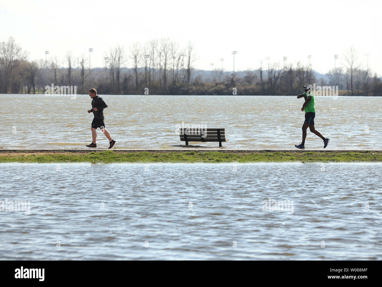 Joggers run on a narrow path between two bodies of water that have flooded at the Creve Coeur