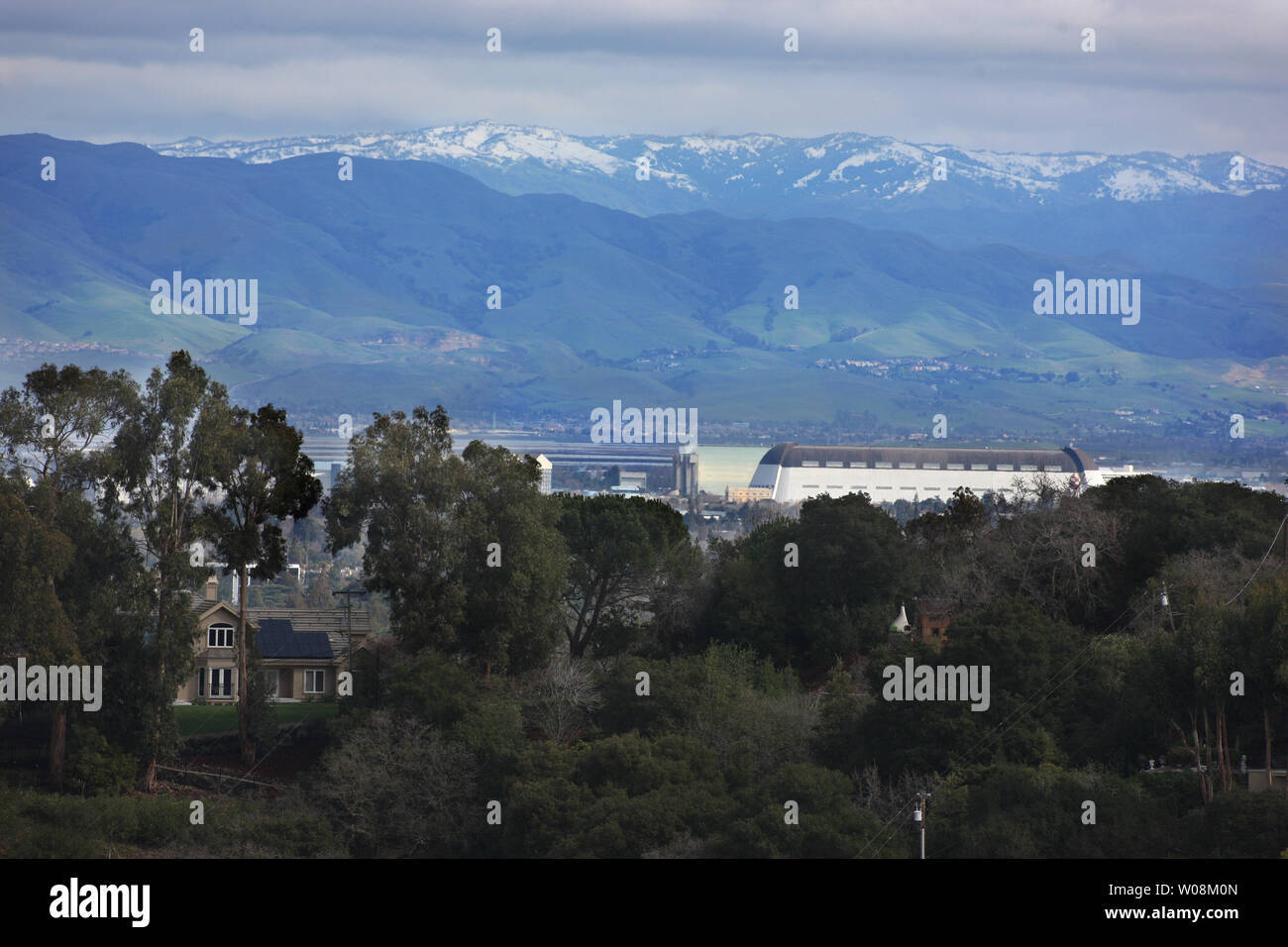 Snow dusts the mountain tops above Silicon Valley as cold temperatures and overnight precipitation pushed the snow line within sight of a house in Palo Alto (L) and the dirigible hanger (R) at Moffett Field, California on February 14, 2009.   (UPI Photo/Terry Schmitt) Stock Photo