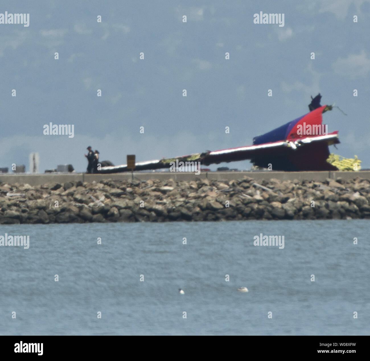 Officials walk past the tail of an Asiana Air Boeing 777 on the runway at San Francisco International Airport after it crashed on landing in San Francisco on July 6, 2013. The plane was arriving from Seoul.    UPI/Terry Schmitt Stock Photo