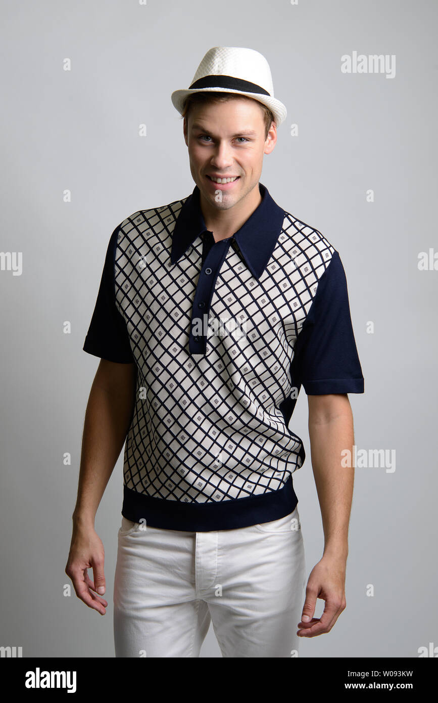 A Brown hair Caucasian male model wearing a white fedora hat, poses in vintage shirt, 60s shirt, a vintage preppy style fashion editorial. Stock Photo