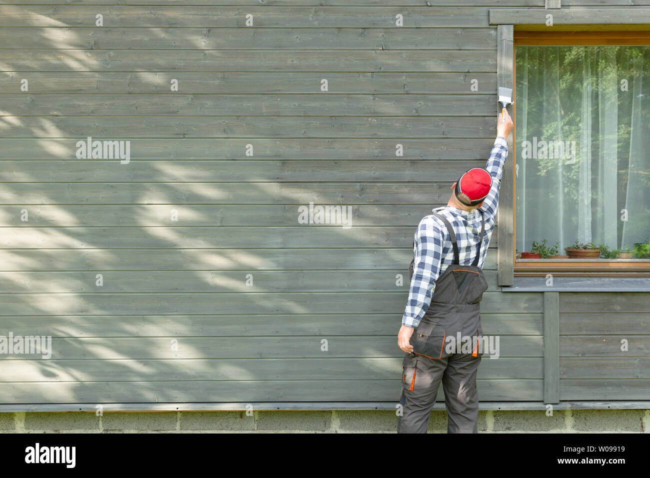 Man worker painting wooden house exterior wall with paintbrush and wood protective color Stock Photo