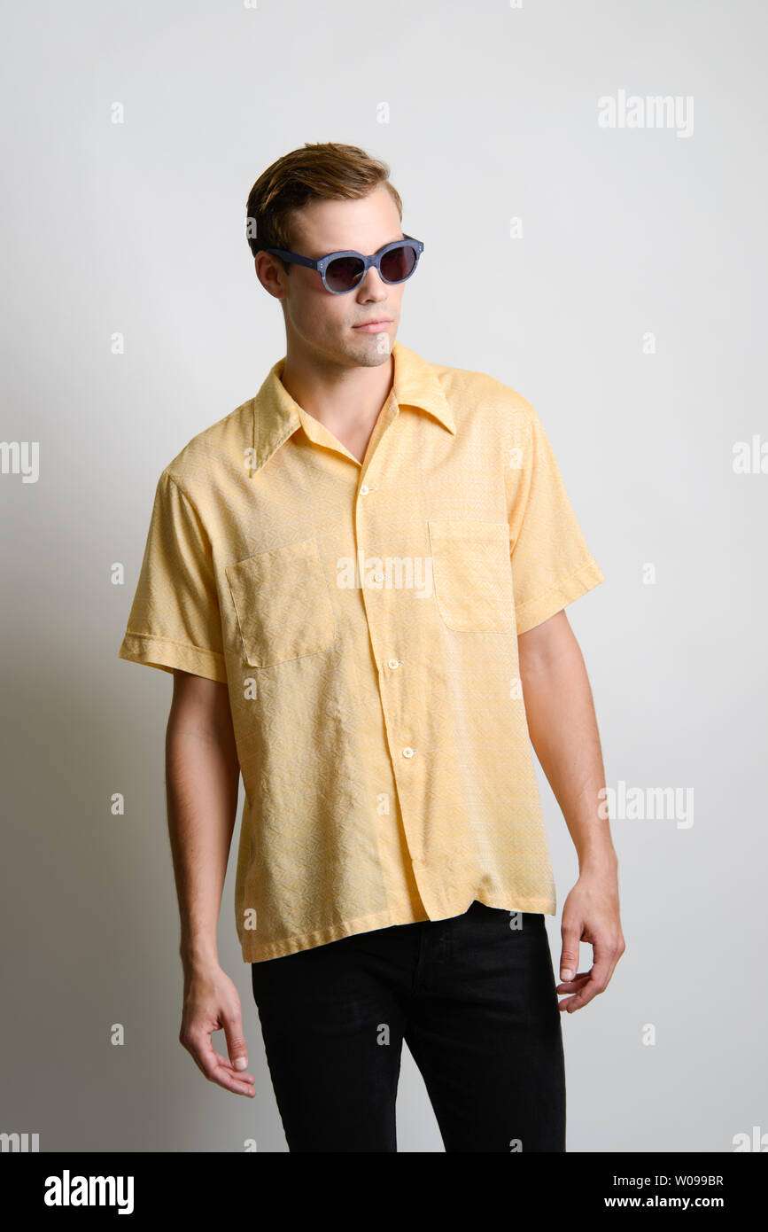 A Brown hair Caucasian male model poses in vintage 70s shirt, yellow shirt. He wears dark sunglasses. A summer editorial. Stock Photo