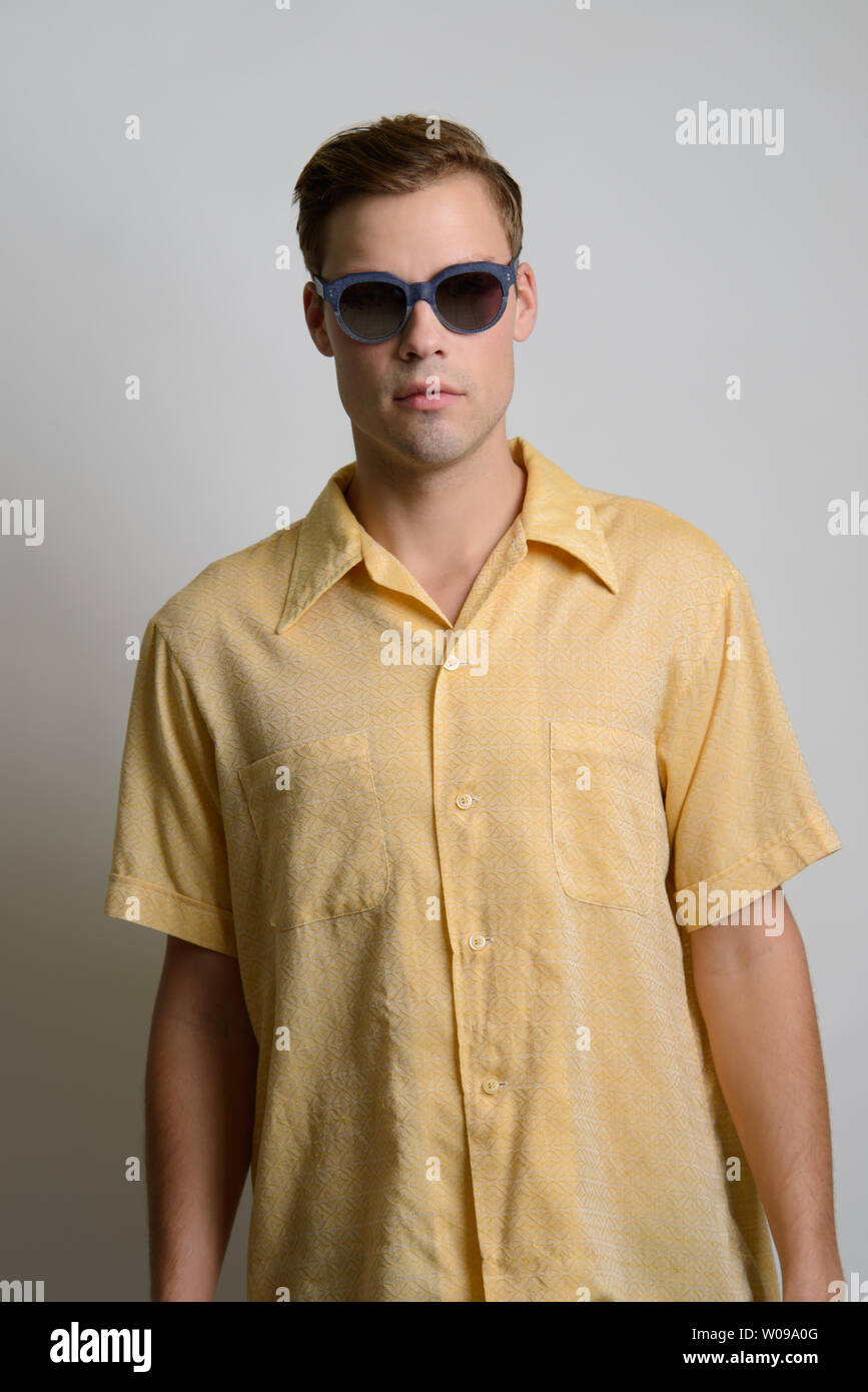 A Brown hair Caucasian male model poses in vintage 70s shirt, yellow shirt. He wears dark sunglasses. A summer editorial. Stock Photo