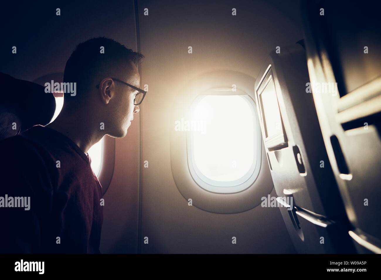 Man traveling by airplane. Pensive passenger looking through window during flight at sunset. Stock Photo