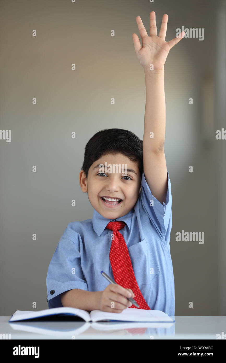 Portrait of a schoolboy raising hand in classroom Stock Photo - Alamy