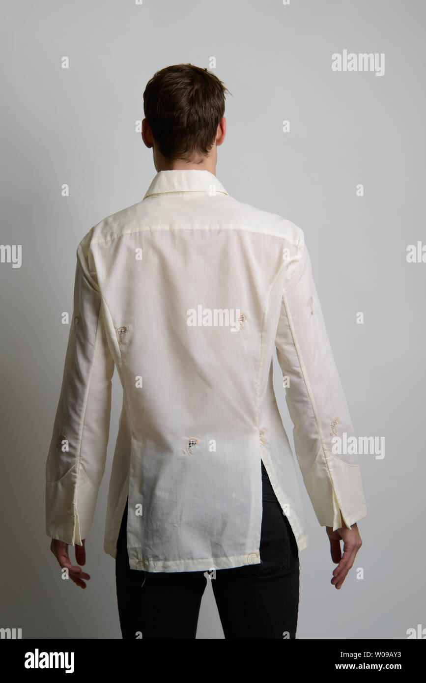 A Brown hair Caucasian male model poses, back facing camera, he wears a cream vintage shirt. Stock Photo