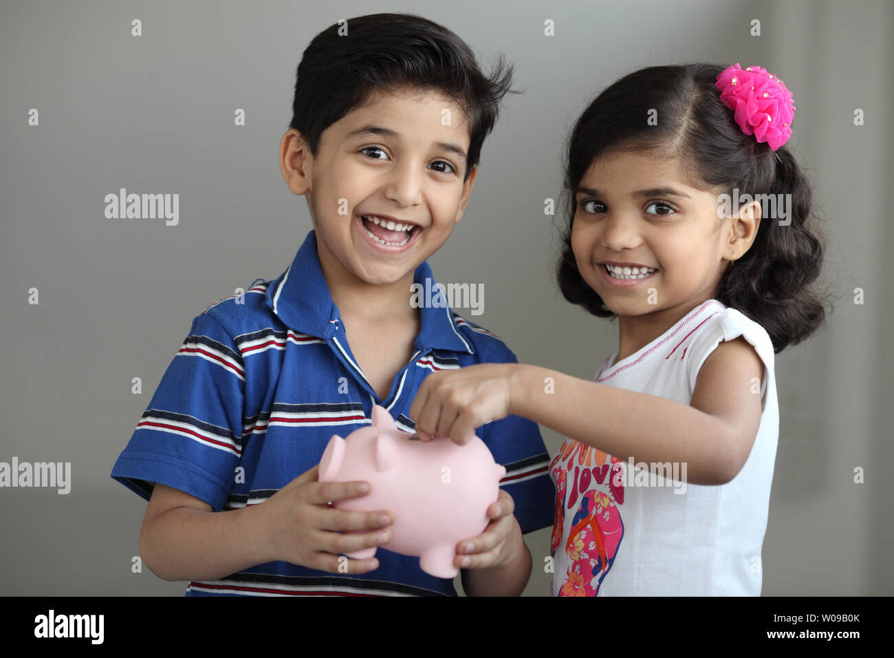 Girl putting coin into a piggy bank with her brother Stock Photo - Alamy