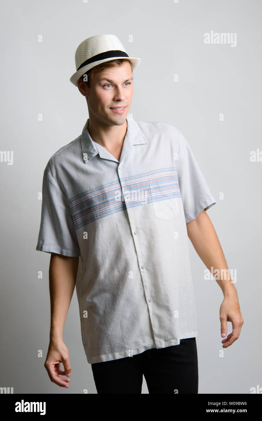 A Brown hair Caucasian male model poses in vintage blue shirt and a white fedora hat smiling. Stock Photo