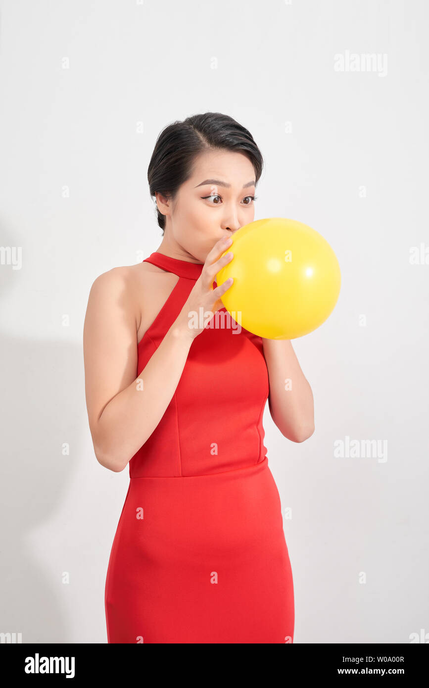 Happy emotional young asian woman in red is blowing a yellow balloon in studio. Portrait of beautiful vietnamese girl. Shopping concept Stock Photo