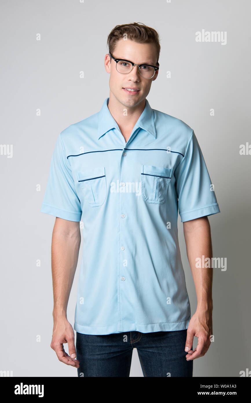 A Brown hair Caucasian male model wearing vintage glasses, poses in a blue vintage 60s shirt, a men's vintage fashion editorial. Stock Photo