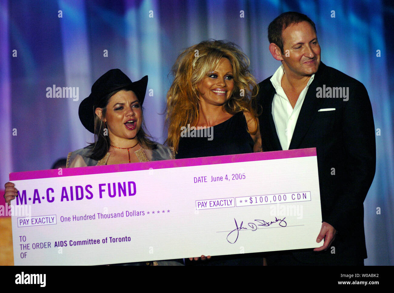 Pamela Anderson (center) and MAC Cosmetics CEO John Demsey present a $100,000 check to the Aids Committee of Toronto during Fashion Cares 2005 MAC Viva Glam Bollywood Cowboy at the Metro Toronto Convention Center in downtown Toronto, Canada on June 4, 2005. The annual fundraising gala event showcases Canadian talent and fashion to benefit the Aids Committee of Toronto and Anderson flew into town for the day to host the night's festivities. (UPI Photo/Christine Chew) Stock Photo