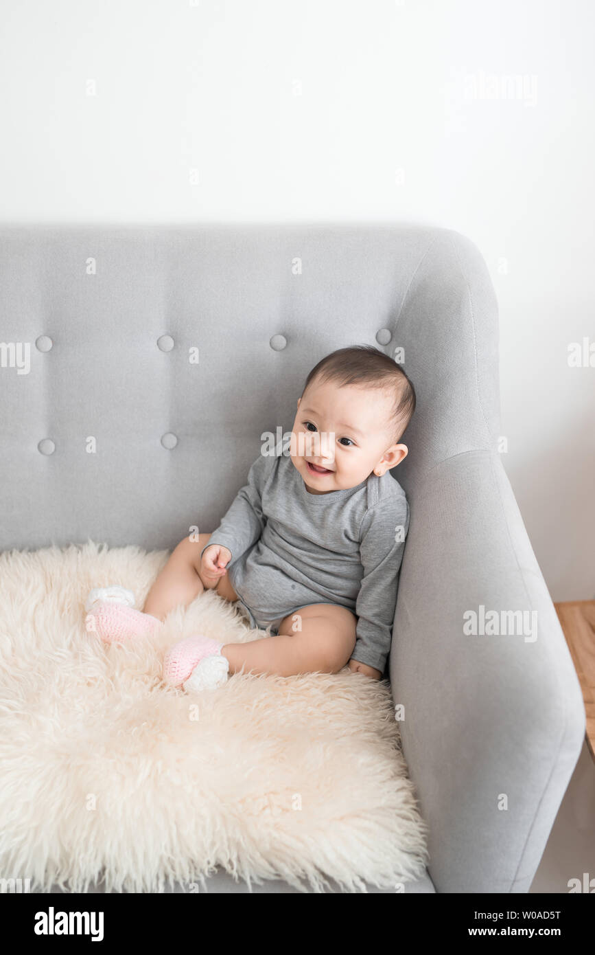 Closeup portrait of cute adorable smiling laughing, baby girl with black  eyes sitting on sofa looking away from camera, natural window light,  lifestyl Stock Photo - Alamy