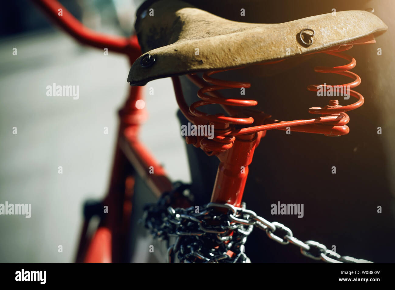A bright red retro bike with an old leather saddle is tied with a metal