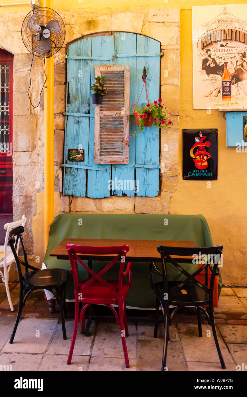 Colourful, painted shutters with pot plants, outside bar seating and table. Larnaca, Cyprus. June 2019 Stock Photo