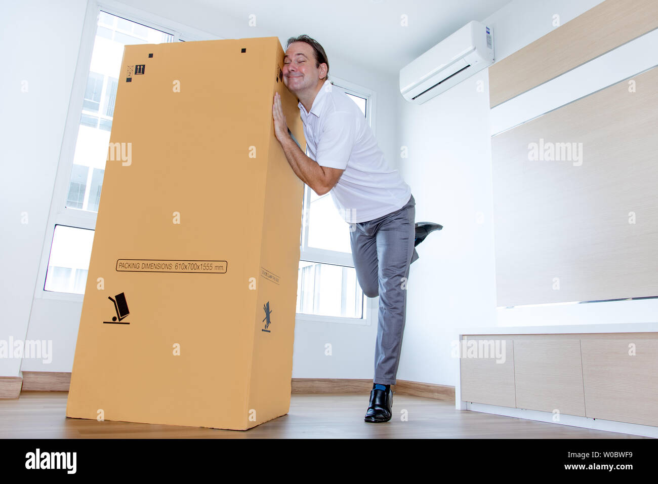 A man likes a big paper box in the apartment. A emotional man fondle a big package in the empty room. Stock Photo
