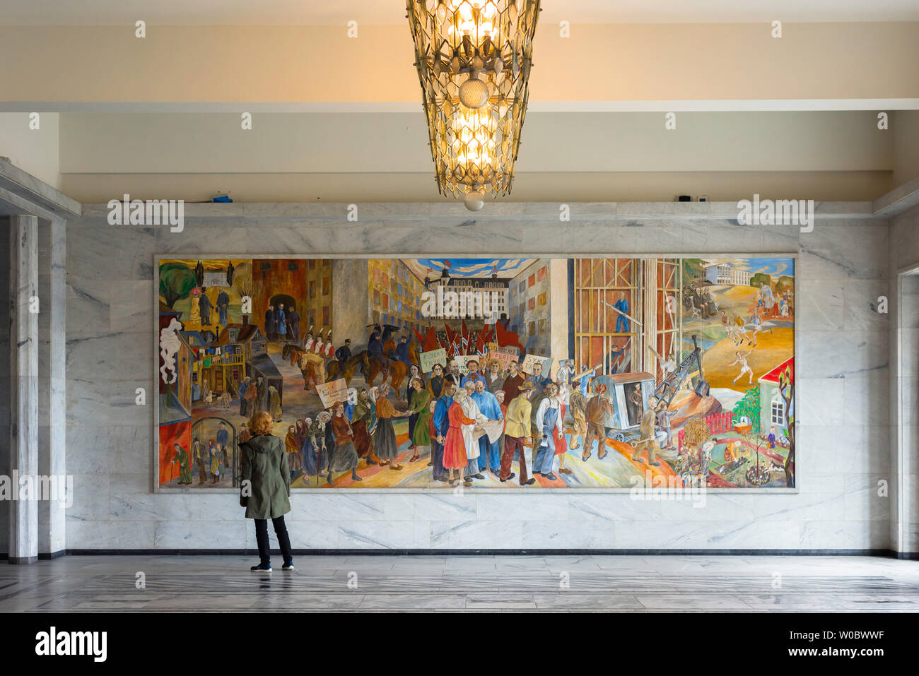 Oslo Town Hall, view of a female tourist looking at a Reidar Aulie painting titled 'The Labor Movement’s Development in Oslo' in the Oslo City Hall. Stock Photo