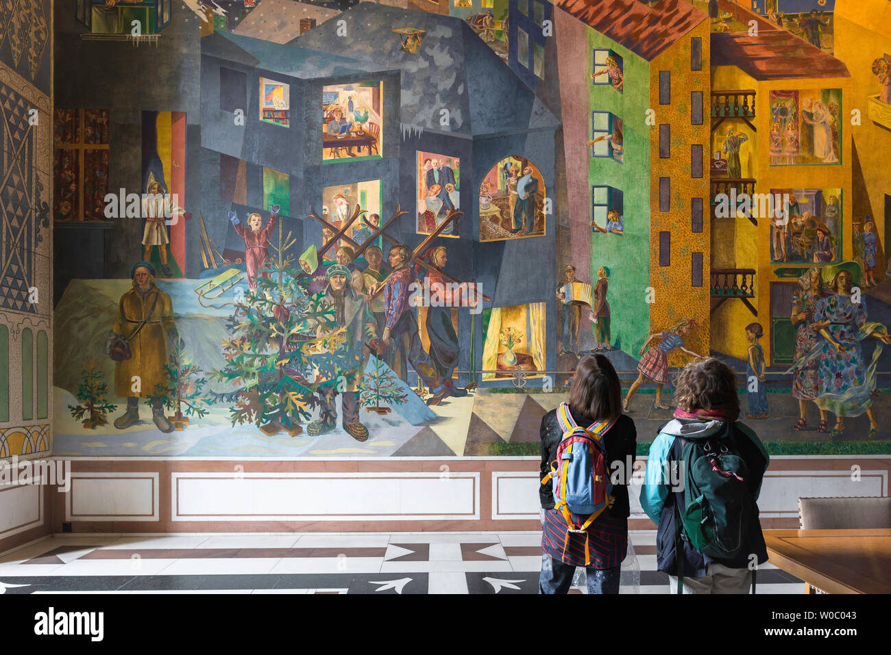 Women travel, rear view of two women with backpacks looking at the colourful Per Krohg fresco inside the East Gallery of Oslo City Hall, Norway. Stock Photo