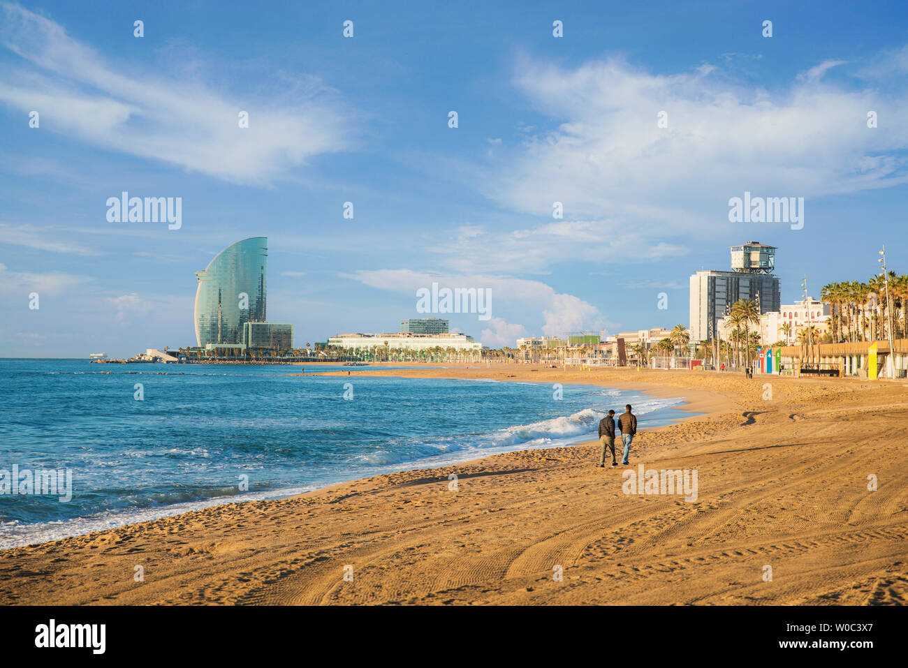 Pedestrians walk along Barceloneta Beach in Barcelona with colorful sky at sunrise. Seafront, beach,coast in Spain. Suburb of Barcelona, Catalonia Stock Photo