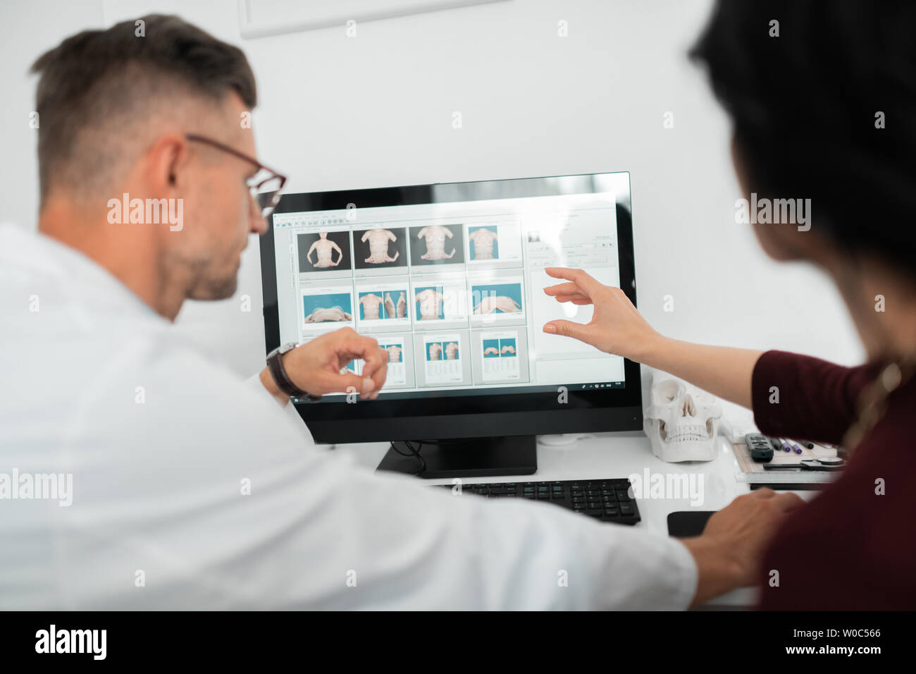 Plastic surgeon wearing glasses consulting client near computer Stock Photo