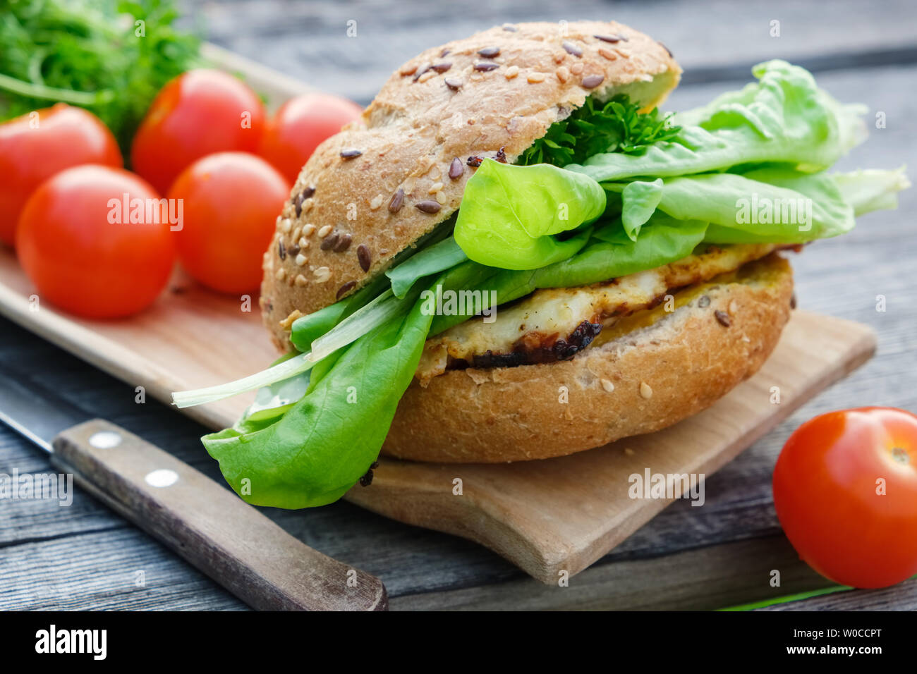 Tasty homemade burger with meat, lettuce, tomatoes, sesame bun on wooden picnic table outdoors. Stock Photo