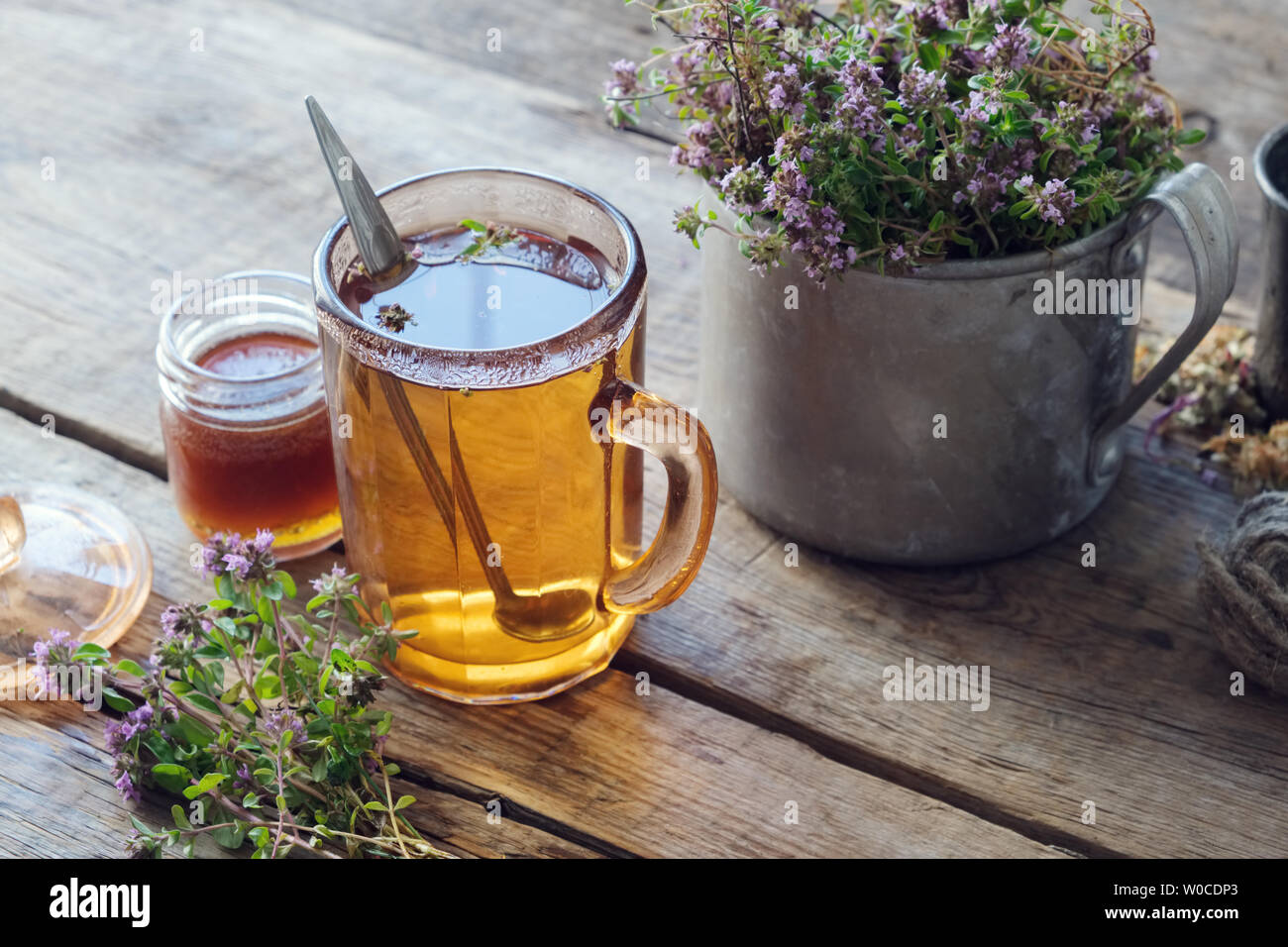 Mug of thyme healthy herbal tea, honey jar and rustic metal cup full of thymus serpyllum medicinal herbs. Stock Photo