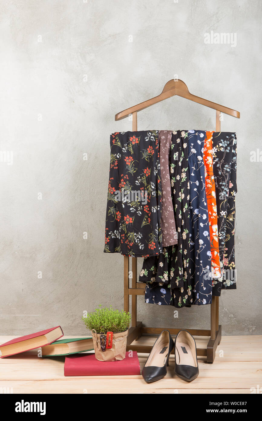 Shopping and style concept - clothes rack with trendy dresses in floral print, shoes and books on wooden floor and grey concrete background. Vertical Stock Photo