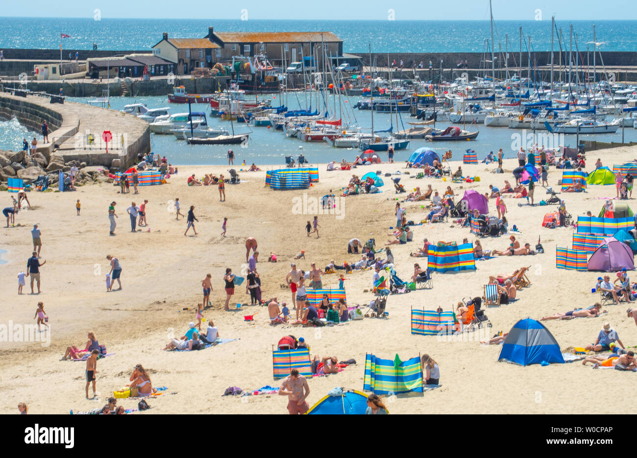Lyme Regis, Dorset, UK. 27th June 2019. UK Weather: Sunseekers flock to the picturesque seaside resort of Lyme Regis to soak up the scorching hot sunshine and bright blue skies as the Saharan heatwave hits the UK. Visitors and locals bask in sweltering sun on the town's sandy beach. Credit: Celia McMahon/Alamy Live News. Stock Photo