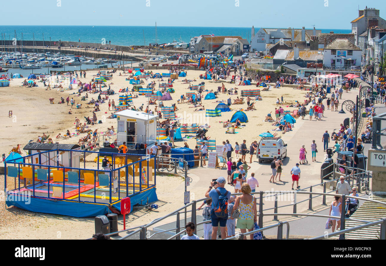 Lyme Regis, Dorset, UK. 27th June 2019. UK Weather: Sunseekers flock to the picturesque seaside resort of Lyme Regis to soak up the scorching hot sunshine and bright blue skies as the Saharan heatwave hits the UK. Visitors and locals bask in sweltering sun on the town's sandy beach. Credit: Celia McMahon/Alamy Live News. Stock Photo