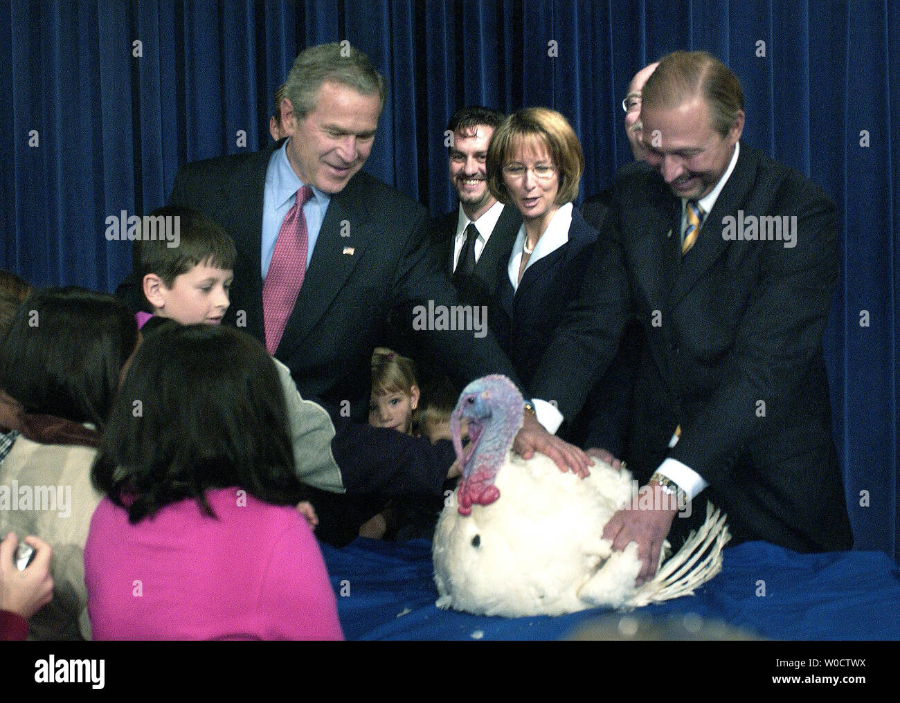 President George W. Bush (L), turkey raiser James Trites (R) and principles and students from various local elementary schools pet the recently pardoned turkey, Marshmallow, during the 58th annual Turkey Ceremony, at the Old Executive Office Building in Washington on November 22, 2005. The Turkey will fly first class to Disneyland where he will serve at the grand marshal of the Disneyland's Thanksgiving Day Parade, and spend the rest of his life at a nature preserve at the park. (UPI Photo/Kevin Dietsch) Stock Photo