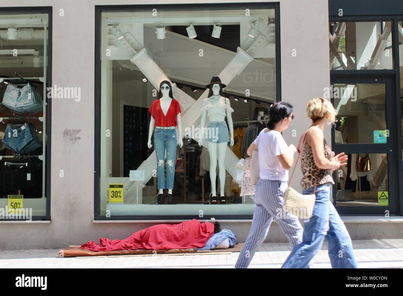 shoppers walk past a sleeping homeless person in central athens ...