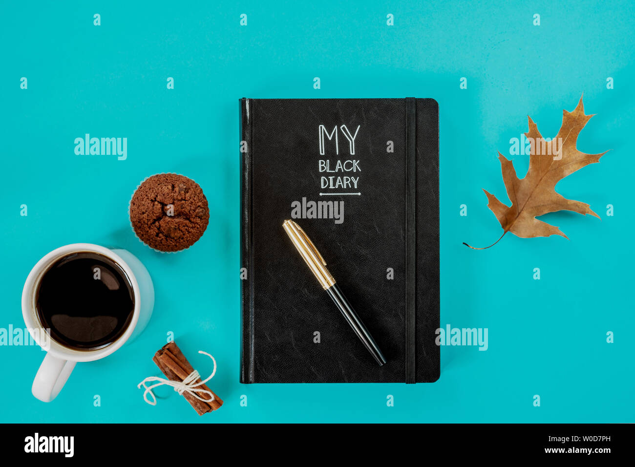 Working concept. Diary, pen, cup of coffee, muffin and fallen leaf on blue background. Top view. Stock Photo