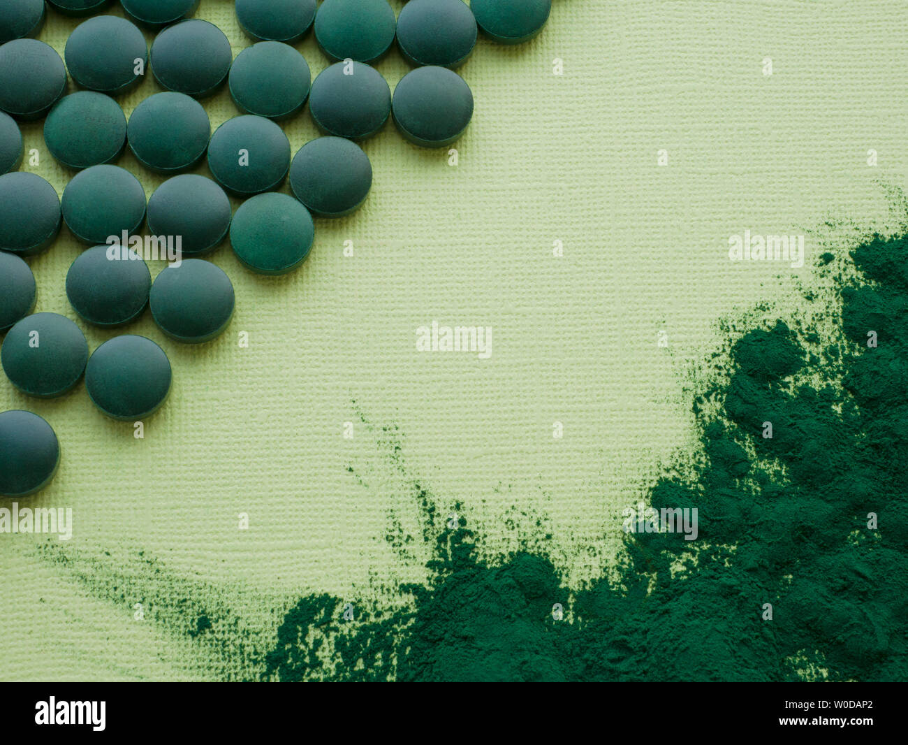 Spirulina algae tablets and powder on green background from top view