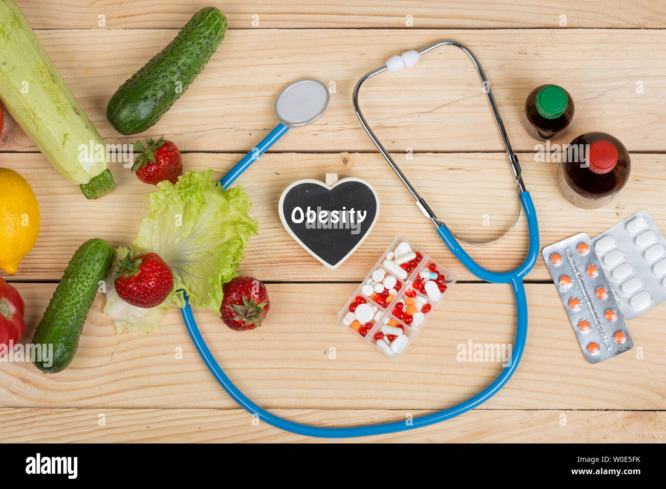 Blackboard in shape of heart with text Obesity, stethoscope and choice between natural vitamins, vegetables, fruits and berries or tablets and pills o Stock Photo