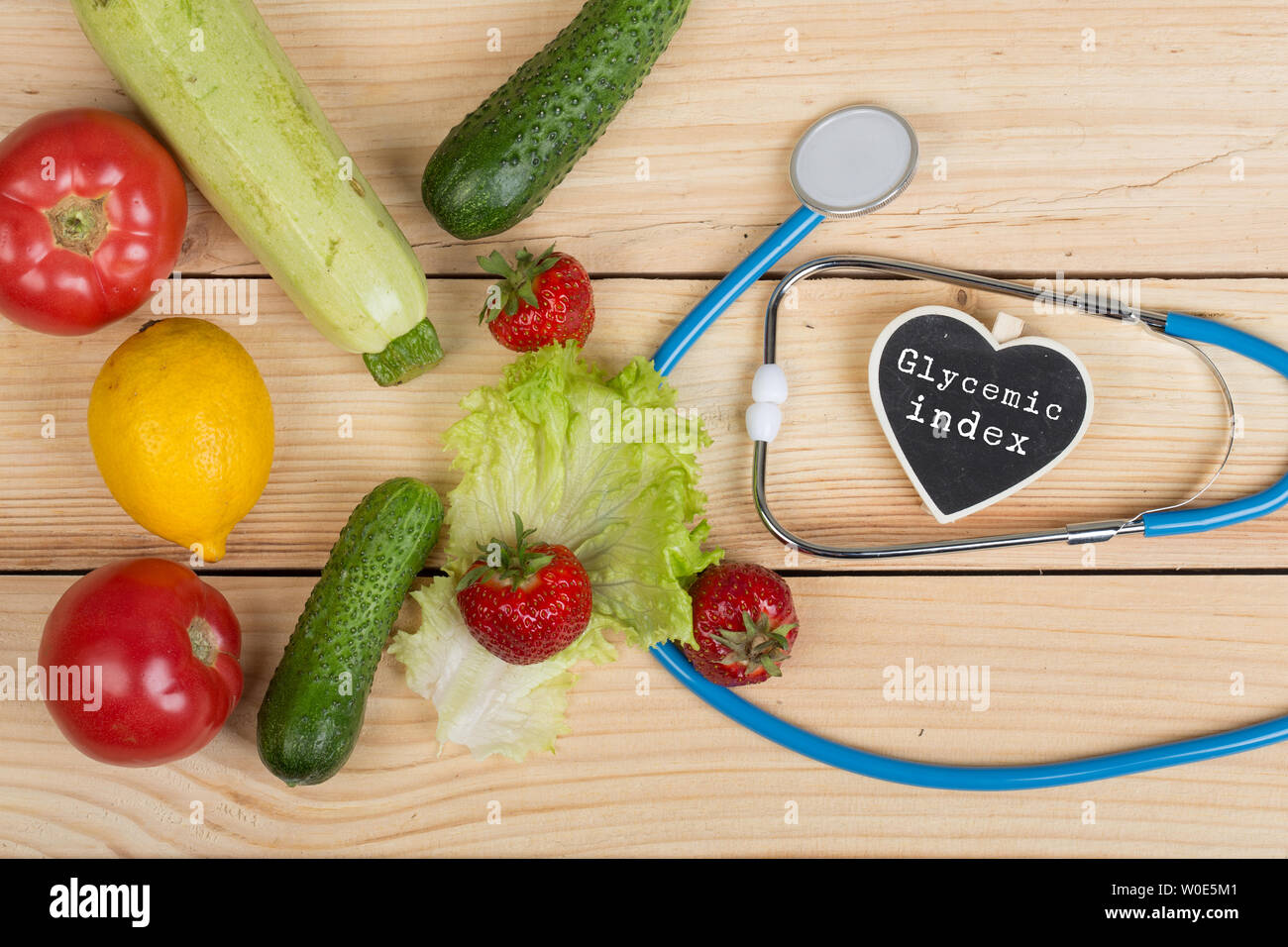 Good healthy and diet concept - Blackboard in shape of heart with text Glycemic index, stethoscope, vegetables, fruits and berries on wooden table Stock Photo