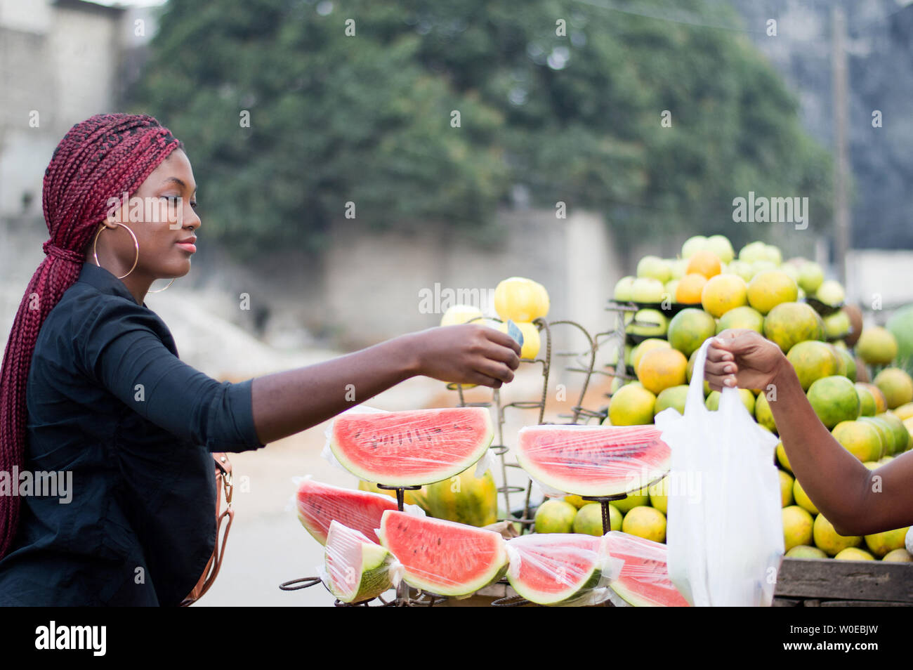 young woman gives a banknote to the vendor at street fruit market. Stock Photo