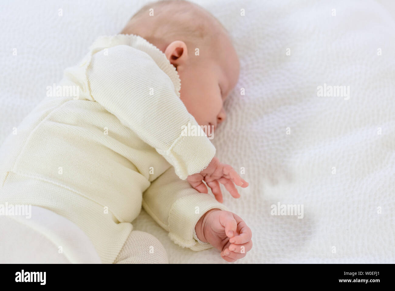 Young infant in white layette of 2 months sleeping on a whitebed. Stock Photo